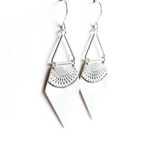 May include: A pair of silver earrings with a geometric design. Each earring features a diamond-shaped bottom, a textured half-circle, and a triangular top connected by a small bar. The earrings hang from a simple hook.