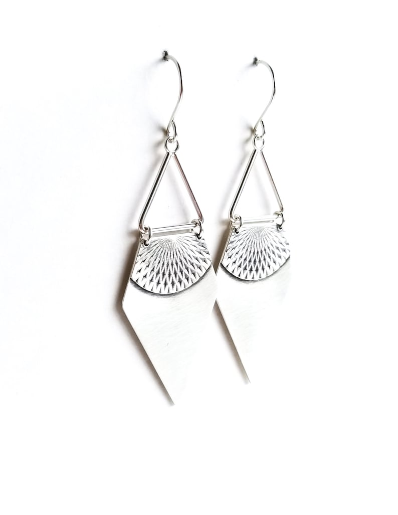 May include: A pair of silver earrings with a geometric design. Each earring features a diamond-shaped bottom, a textured half-circle, and a triangular top connected by a small bar. The earrings hang from a simple hook.