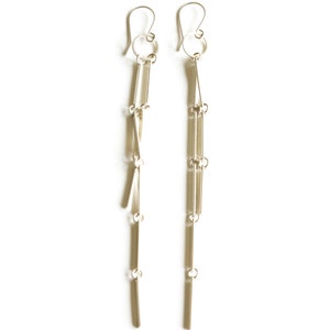 Peut inclure: Une paire de boucles d'oreilles pendantes argent&eacute;es. Chaque boucle d'oreille comprend un crochet, un petit anneau et plusieurs &eacute;l&eacute;ments rectangulaires et en forme de barre reli&eacute;s par de petits anneaux, cr&eacute;ant un effet superpos&eacute;. Fond blanc.