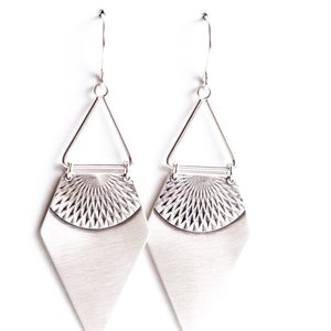 May include: A pair of silver-toned earrings. Each earring features a geometric design with a triangular top, a textured semi-circle, and a diamond-shaped bottom. The earrings hang from a simple hook.