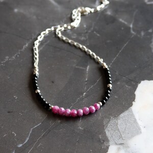 May include: A silver chain necklace with a beaded design. The necklace features a combination of black and pink beads, with a silver chain. The beads are arranged in a curved pattern, creating a stylish accessory.