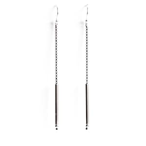 May include: A pair of silver-toned dangle earrings. Each earring features a delicate chain that suspends a slender, cylindrical bar. The earrings have a simple, minimalist design, with a small bead at the end of each bar.