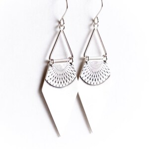 May include: A pair of silver earrings with a geometric design. Each earring features a diamond-shaped bottom, a textured half-circle, and a triangular top connected to a hook. The earrings are displayed against a white background.