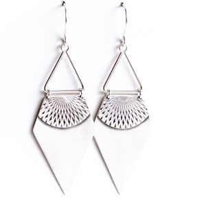 May include: A pair of silver-toned earrings. Each earring features a geometric design with a triangular top, a textured semi-circle, and a diamond-shaped bottom. The earrings hang from a simple hook.
