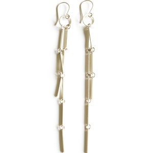 Peut inclure: Une paire de boucles d'oreilles pendantes argent&eacute;es. Chaque boucle d'oreille comprend un crochet, un petit anneau et plusieurs barres rectangulaires verticales reli&eacute;es par de petits anneaux, cr&eacute;ant un design lin&eacute;aire et fluide. Sur fond blanc.