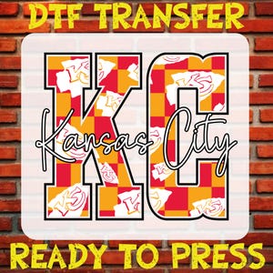 May include: A red and yellow checkered design with the letters "KC" in black outlined in white. The letters are filled with a pattern of white "KC" logos on a red and yellow background. The words "Kansas City" are written in white cursive script below the letters. The words "DTG Transfer" are written in yellow at the top of the image. The words "Ready To Press" are written in yellow at the bottom of the image.