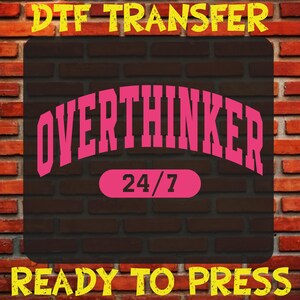 May include: A DTF transfer design featuring the word "OVERTHINKER" in pink, arched over a pink oval with "24/7". The design is set against a dark brown brick background, with yellow text at the top and bottom that reads "DTF TRANSFER" and "READY TO PRESS".