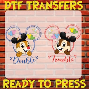 May include: Two iron-on transfers featuring Chip 'n Dale in Mickey Mouse ears with balloons and Tinkerbell. The left transfer says "Double" in blue text and the right transfer says "Trouble" in red text. Both transfers are ready to press.