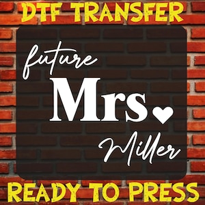May include: A DTF transfer design featuring the text "future Mrs. Miller" in white script with a heart symbol, set against a dark brick backdrop. The words "DTF TRANSFER" and "READY TO PRESS" are in yellow.