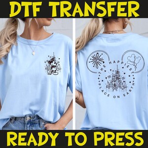 May include: Light blue t-shirt featuring a black and white graphic of Mickey Mouse in front of a castle on the front. The back of the shirt has a castle design with the text "The Happiest Place on Earth". The words "DTF TRANSFER" and "READY TO PRESS" are in yellow and black.