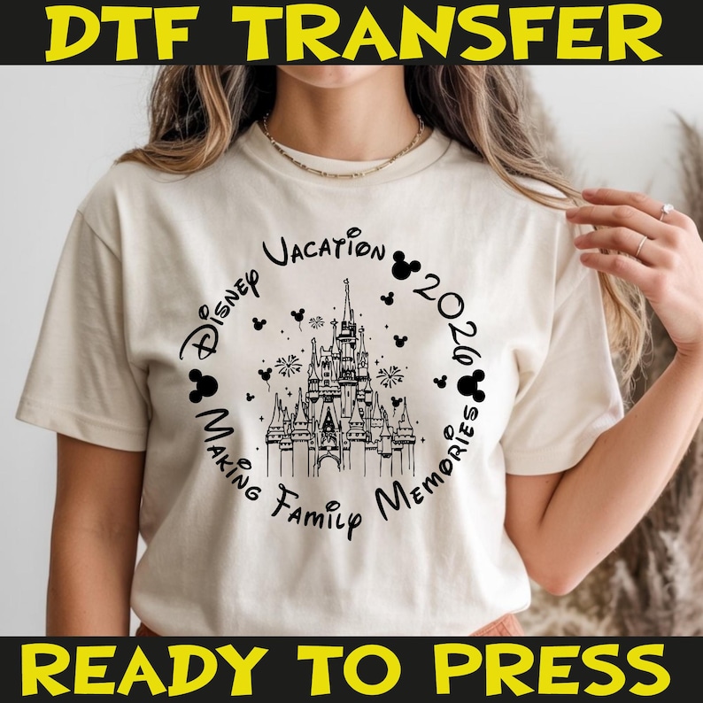 K&ouml;nnte beinhalten: Cremefarbenes T-Shirt mit schwarzem Grafikdesign. Das Design enth&auml;lt den Text "Disney Vacation 2026 Making Family Memories", der eine detaillierte Illustration eines Schlosses umgibt. Mickey Mouse-Silhouetten und Feuerwerk erg&auml;nzen das Design.