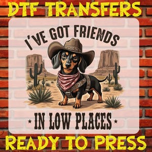 May include: A digital transfer design featuring a cartoon dachshund wearing a cowboy hat and bandana with the text "I've got friends in low places". The design is set against a desert landscape with cacti and mountains. The text "DTF Transfers Ready to Press" appears at the top and bottom of the design.