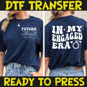May include: Navy blue t-shirt with white text that reads "FUTURE Mrs. Martinez" on the front and "IN MY ENGAGED ERA" on the back. The shirt features a diamond ring graphic and is ready to press.