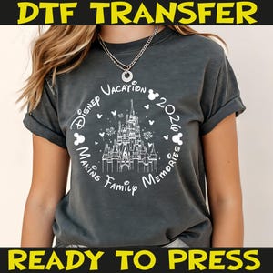 K&ouml;nnte beinhalten: Dunkelgraues T-Shirt mit einem wei&szlig;en Aufdruck eines Schlosses, Mickey Mouse-K&ouml;pfen und dem Schriftzug "Disney Vacation 2020 Making Family Memories". Das Shirt hat hochgekrempelte &Auml;rmel und die gelben Schriftz&uuml;ge "DTF TRANSFER" und "READY TO PRESS".
