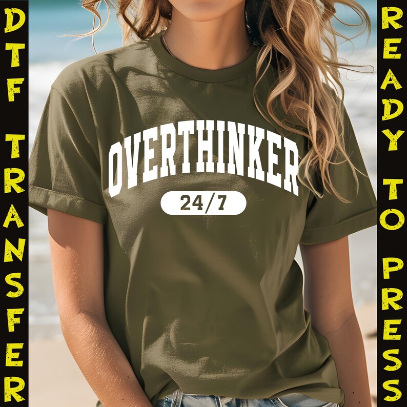 May include: Olive green t-shirt with the white text "OVERTHINKER" arched across the top and "24/7" in a white oval below. The shirt has rolled-up sleeves and is ready to press.