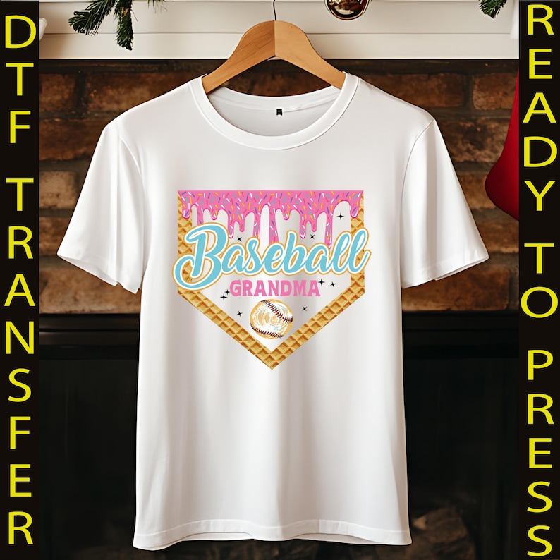 May include: White t-shirt with a pink and blue baseball graphic. The graphic features a baseball diamond with a dripping pink icing design and the text "Baseball Grandma".