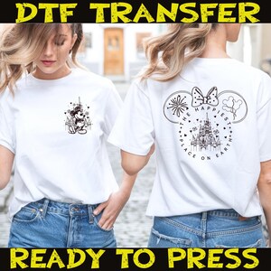 May include: White t-shirts with DTF transfer designs. One shirt features Mickey Mouse in front of a castle, the other has a castle design with the text "The Happiest Place on Earth". The text "DTF TRANSFER" and "READY TO PRESS" are also visible.