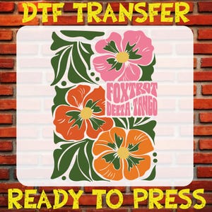 May include: A ready-to-press iron-on transfer featuring a floral design with three flowers in shades of orange, pink, and yellow. The text "FOXTROT DELTA TANGO" is centered in the design.