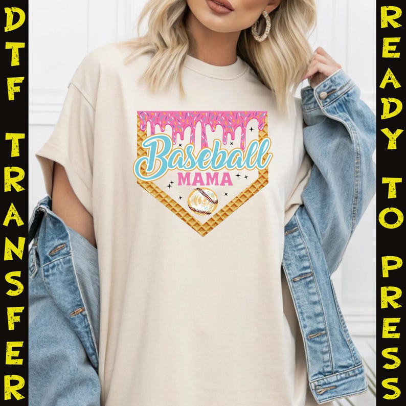May include: A beige t-shirt with a pink and blue graphic of a baseball home plate with the text "Baseball Mama" and a baseball inside the plate.