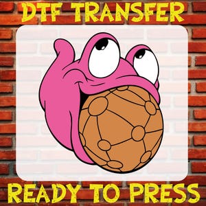 May include: A pink cartoon character with large eyes and a wide grin, holding a brown ball with a network of lines. The words "DTF TRANSFER" and "READY TO PRESS" are in yellow text.