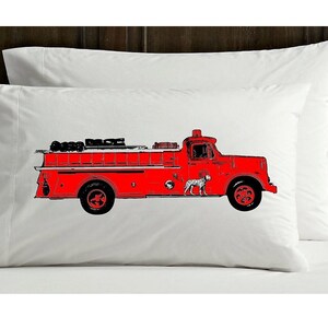 May include: A red fire truck with black detailing and a white dalmatian dog on the side. The truck is on a white pillowcase.
