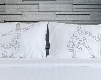May include: Two white pillowcases with black line drawings of soccer players. One pillowcase shows a player kicking a ball, the other shows a goalie diving to catch a ball.