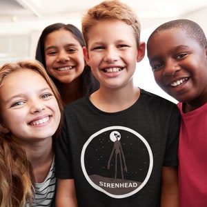 May include: A group of five children smiling for the camera. The child in the center is wearing a black t-shirt with a white circle graphic of a tall, slender figure with a long, thin head and a moon in the background. The text "SIRENHEAD" is printed below the graphic.