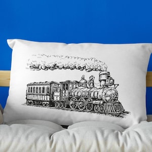 May include: A white pillow with a black and white illustration of a steam train with smoke coming from the chimney. The pillow is on a light brown wooden couch with a pink blanket draped over the back.