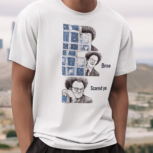 May include: White t-shirt featuring a graphic of a man with the text "Bree Scared ya". The graphic is a black and white illustration of the man in three different poses. The shirt is made of a soft material.