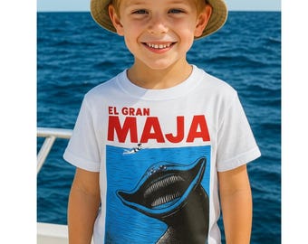 May include: A young person wearing a white t-shirt with the text "EL GRAN MAJA" in red letters. The shirt features a blue graphic of a marine animal. The person is also wearing a beige bucket hat.
