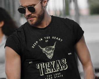 May include: A black t-shirt with a vintage-style graphic design featuring a Highland cow and the text "Deep in the heart of Texas, Est. 1845, The Lone Star State".
