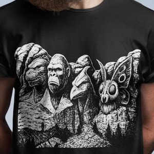 Puede incluir: Camiseta negra con un gr&aacute;fico en blanco y negro que representa cuatro criaturas, incluyendo una tortuga, un simio, un p&aacute;jaro y una polilla, talladas en una monta&ntilde;a. La camiseta la lleva una persona con barba y gafas de sol.