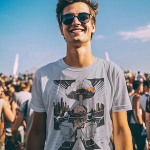 May include: A white t-shirt with a graphic design featuring a mushroom cloud over a city skyline. The shirt is worn by a person wearing sunglasses, smiling, and standing in a crowd under a blue sky.