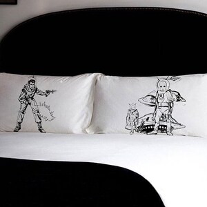 May include: A white bed with black and white pillowcases featuring illustrations of astronauts and spaceships. The bed has a black headboard and a black blanket.