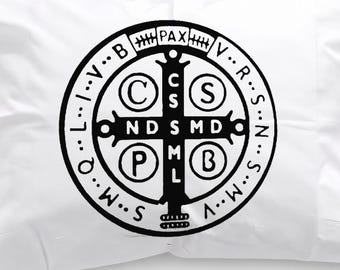 May include: A rectangular white pillowcase featuring a centred black Saint Benedict medal graphic. The circular design includes a cross with the letters C S S M L and N D S M D, along with the word PAX at the top and various letters around the border.