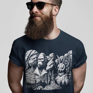 Puede incluir: Camiseta azul marino con un dise&ntilde;o gr&aacute;fico en blanco y negro de cuatro criaturas talladas en una monta&ntilde;a. Las criaturas son una tortuga, un gorila, un p&aacute;jaro y una polilla. Cuello redondo.