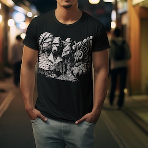 Puede incluir: Camiseta negra con un gr&aacute;fico blanco que representa un monumento con tem&aacute;tica de primates. El dise&ntilde;o incluye caras de gorilas y otros animales talladas en una estructura monta&ntilde;osa. La camiseta la lleva una persona con vaqueros azul claro.