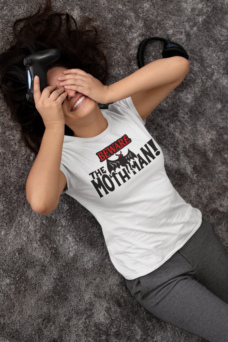 May include: A white t-shirt with a black graphic that says "Beware the Mothman!" with a black silhouette of a mothman with red eyes.
