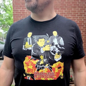 Peut inclure: Un t-shirt noir avec un imprim&eacute; graphique d'un groupe d'hommes en costume et un pistolet. Le texte "Threat Level Midnight" est imprim&eacute; sous l'image.