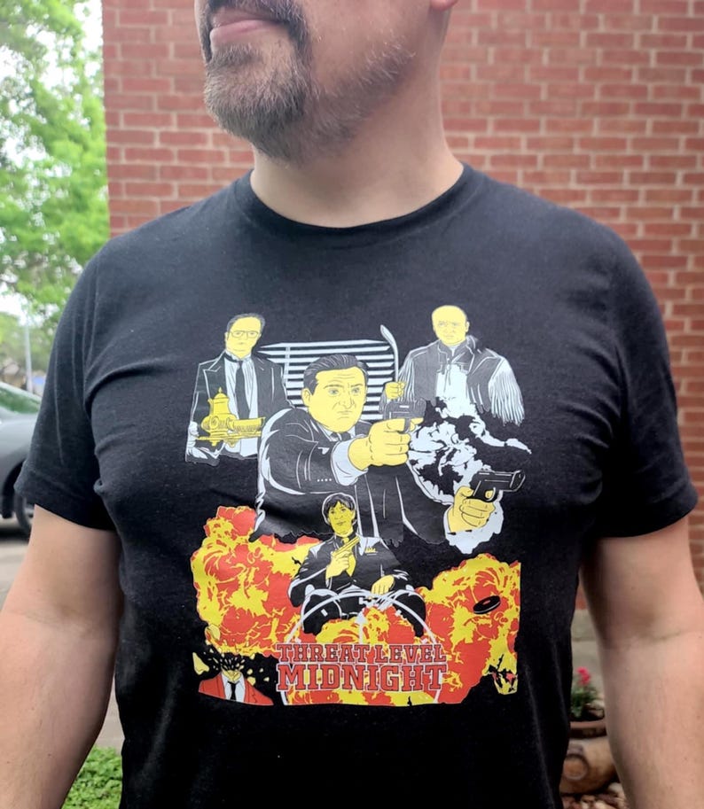Peut inclure: Un t-shirt noir avec un imprim&eacute; graphique d'un groupe d'hommes en costume et un pistolet. Le texte "Threat Level Midnight" est imprim&eacute; sous l'image.
