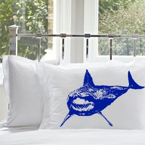 May include: Two white pillowcases with a blue shark silhouette printed on one of the pillowcases.