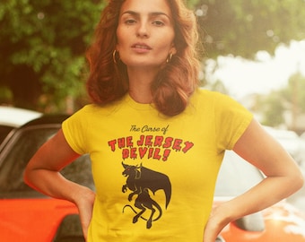 May include: A yellow t-shirt with a black and red graphic of a creature with the text "The Curse of The Jersey Devil!"