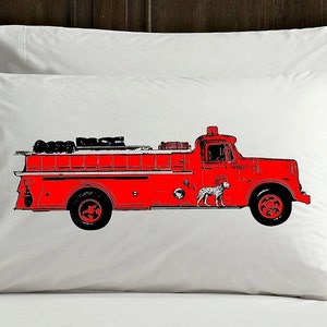 May include: A red fire truck with a black and white illustration of a dog on the side. The truck has a ladder on the back and is on a white pillowcase.