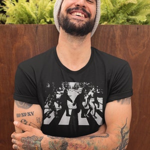 Puede incluir: Una camiseta negra con un gr&aacute;fico de cuatro figuras caminando por un paso de cebra, similar a la portada del &aacute;lbum Abbey Road de los Beatles. Las figuras est&aacute;n estilizadas para parecerse a Bigfoot.