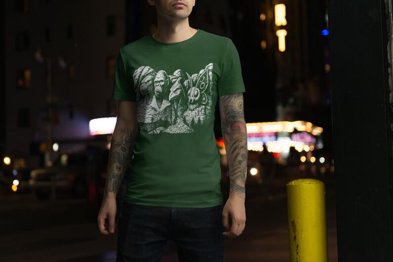 Puede incluir: Camiseta verde con un gr&aacute;fico blanco de criaturas estilizadas, incluyendo un gorila, un conejo y una polilla. La camiseta est&aacute; hecha de un material suave y es adecuada para ropa casual.