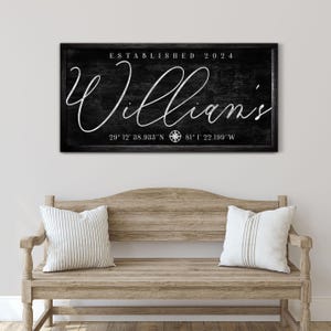 May include: A black wooden sign with the name "Williams" in white script, established in 2024. Coordinates are displayed below the name. The sign hangs above a wooden bench with two striped pillows.