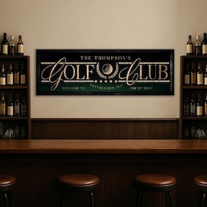 May include: A framed sign with the text "THE THOMPSON'S GOLF CLUB" in gold lettering. The sign includes a golf ball graphic and the words "WELCOME TO" and "THE 19TH HOLE". The sign is displayed above a bar with stools and shelves of wine bottles.