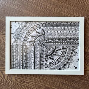 Può includere: Una stampa d'arte mandala in bianco e nero incorniciata con intricati motivi geometrici. Il design presenta un motivo circolare con un punto centrale e linee radianti.