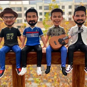 May include: Four figurines of people sitting on a wooden railing. The person on the left is wearing a black shirt with the number 67 on it, blue jeans, and a black hat. The person in the middle is wearing a blue and white striped shirt, black pants, and a black hat. The person on the right is wearing a brown shirt with a pattern, blue jeans, and a black hat. The person on the far right is wearing a white shirt, black pants, and a black hat. The person in the middle is holding a brown guitar.
