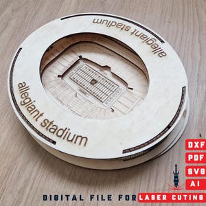Könnte beinhalten: Ein geschichtetes Holzmodell des Allegiant Stadiums. Das Stadion ist kreisförmig mit den Worten "allegiant stadium" am Rand eingraviert. Das Spielfeld und die Sitzplätze sind im Stadion sichtbar. Das Bild enthält auch den Text "DIGITAL FILE FOR LASER CUTTING".